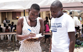 Global Health Economics Ltd - A female youth signing for the benefits card on the project launch day in Kifumbira slum community, Kampala, Uganda .